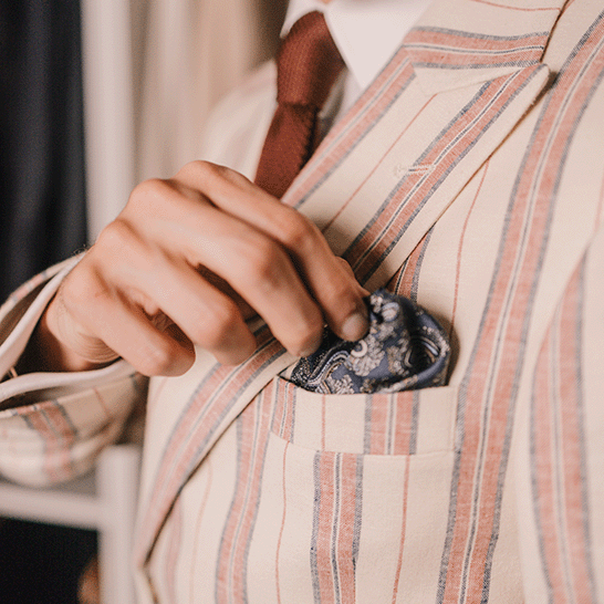 A man in his dressing room adjusting his pocket square to ensure his outfit looks perfect